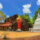 Buddhist temple complex in Sri Lanka with golden Buddha statue, white stupa, red-roofed shrine building, and massive rock for